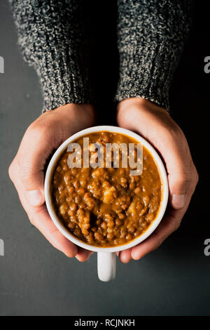 Hohe Betrachtungswinkel und einer jungen kaukasischen Mann mit einer Schüssel mit Linsensuppe in der Hand auf einem grauen Tabelle Stockfoto