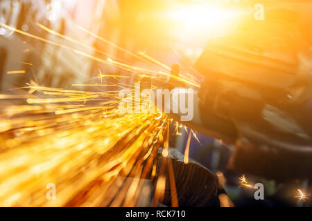 Nahaufnahme eines Mannes sägen Metall Lager mit einer Handkreissäge, helle Blitze fliegen in verschiedenen Richtungen, im Hintergrund Tools für ein Auto Stockfoto