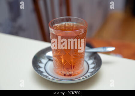 Ein Glas schwarzen Tee. Gemusterte und Löffel. Tee in ein Glas Schale auf einem blured Hintergrund-Bild. Nagel und Kaffee in die Tasse. Stockfoto