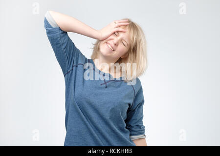 Junge blonde Frau mit blauen pulover mit Hand überrascht auf dem Kopf für Fehler, denken Sie daran, Fehler. Passwort, schlechtes Gedächtnis Konzept. Stockfoto