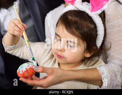 Ostereiersuche auf Frühling Urlaub. Kleines Mädchen mit Eltern malen Ostereier. Familie Liebe Ostern. Frohe Ostern. Kindheit. Kaninchen Familie mit Hasenohren. Funny Bunny. Ostern kommt Stockfoto