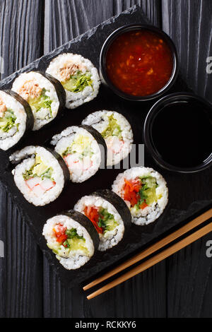 Futomaki brötchen mit verschiedenen Füllungen sind mit Saucen in der Nähe serviert auf einem Schiefer Board auf dem Tisch. Vertikal oben Ansicht von oben Stockfoto