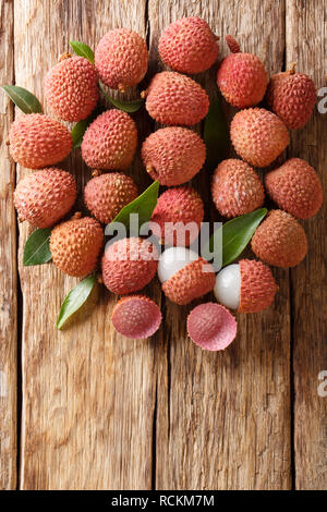 Reif lychee Früchte mit grünen Blättern close-up auf Holz- Hintergrund. Vertikal oben Ansicht von oben Stockfoto