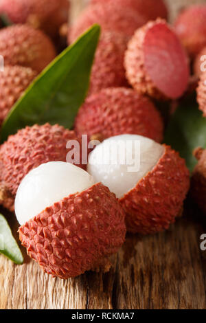 Reif lychee Früchte mit grünen Blättern close-up auf Holzuntergrund. Vertikale Stockfoto