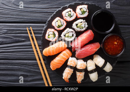 Japanisches Sushi essen. Maki ands Brötchen mit Thunfisch, Lachs, Garnelen, Krabben und Avocado mit zwei Saucen close-up auf einer Schiefertafel Platte. horizontale Ansicht von oben aus einer Stockfoto