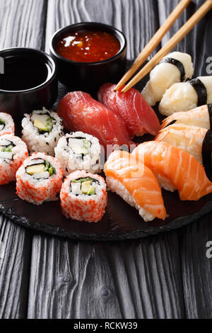 Japanisches Sushi essen serviert auf Tafel, Platte mit zwei Saucen. Sushi Roll mit Garnelen, Avocado, Lachs, Thunfisch, Sesam close-up. Vertikale Stockfoto