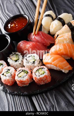 Japanisches Sushi essen. Maki ands Brötchen mit Thunfisch, Lachs, Garnelen, Krabben und Avocado mit zwei Saucen close-up auf einer Schiefertafel Platte. Vertikale Stockfoto