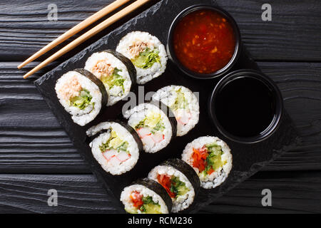 Futomaki brötchen mit verschiedenen Füllungen sind mit Saucen in der Nähe serviert auf einem Schiefer Board auf dem Tisch. horizontal oben Ansicht von oben Stockfoto