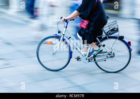 Ältere Frau reitet ein Fahrrad in der Stadt mit der Bewegungsunschärfe Stockfoto