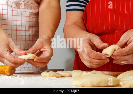 Close-up. Eine ältere Frau in einem roten Küche Schürze macht Kuchen mit einer erwachsenen Tochter Stockfoto