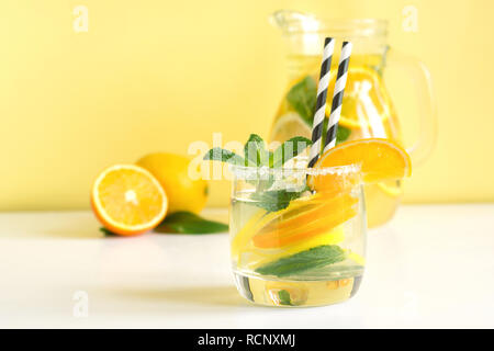 Sommer erfrischende detox Limonade mit Zitrone, Orange, Minze und Eis im Glas auf Gelb. Sommer detox Drinks. Stockfoto