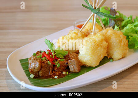 Geschlossen bis Sauteed Rindfleisch und Frittierte klebrige Reisbällchen mit frischem Salat in einer weißen Platte auf hölzernen Tisch Stockfoto