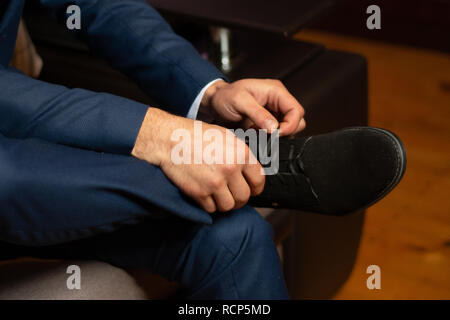 Ein zukünftiger Ehemann verschärft für eine Hochzeit, indem Sie auf seine Schuhe und seine Krawatten binden. 2019 Stockfoto