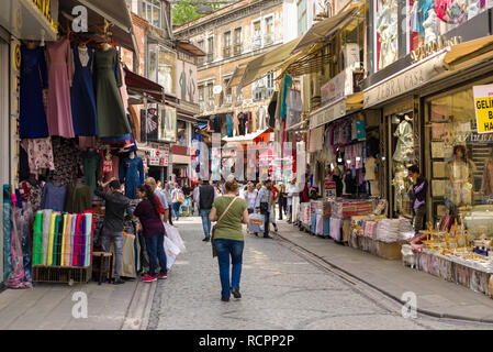 Reihen von Läden mit Waren auf Zeile einer hügeligen Straße mit Kopfsteinpflaster mit Menschen und Touristen spazieren im Stadtteil Fatih, Istanbul, Türkei Stockfoto