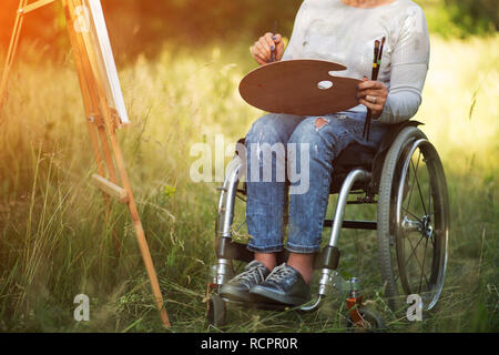 Frau im Rollstuhl Zeichnung auf staffelei außerhalb Stockfoto