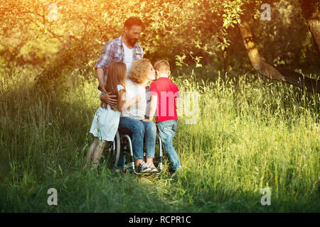 Frau im Rollstuhl küsst ihr Sohn unter Familienmitgliedern Stockfoto