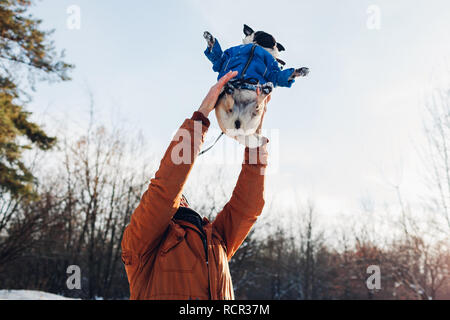 Mops Hund wandern mit seinem Meister im Winter Wald. Der Mensch seinem Haustier wirft für Spaß. Welpen tragen Winter Mantel. Stockfoto