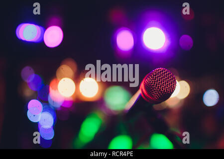 Das Mikrofon auf einem Ständer bereit für Live-Musik oder Karaoke Nacht mit weichen bokeh Lichter und Menschen Silhouetten im Hintergrund. Konzept für die musikalische Veranstaltung singen, eine gute Zeit zu haben. Stockfoto