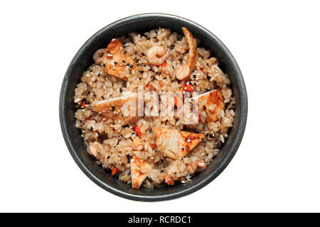 Reis mit gebratenes Huhn, Garnelen, Gemüse und Sesam im schwarzen Schüssel. Auf weissem Hintergrund. Leckeres Restaurant Dish. Stockfoto
