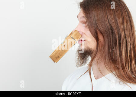 Mann mit Clip-Peg Wäscheklammer auf der Nase. Junge langhaarige Kerl Gefühl unangenehmer Geruch Gestank. Schlechter Geruch Konzept. Stockfoto