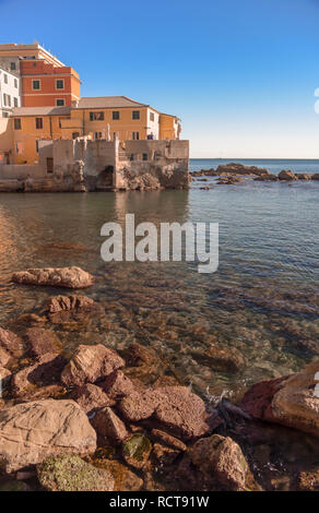 Malerischer Blick auf bunte Häuser in boccadasse an der italienischen Riviera in Ligurien mit glitzerndem Sonnenlicht auf dem Meer und Felsen im Vordergrund. Stockfoto