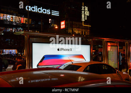 Peking, China - November 11, 2017: Night Shot in Sanlitun, einer geschäftigen Einkaufsstraße, mit Reklametafeln ad für die Freigabe, wenn das iPhone X. Adidas und Uniq Stockfoto