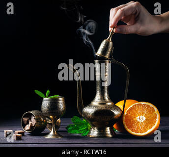 Marokkanischen Tee mit Minze und Orangen in orientalischen Cooper pot und Tassen auf rustikalen Holzmöbeln Hintergrund Stockfoto