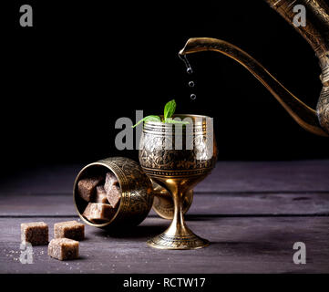 Marokkanischen Tee mit Minze gießen aus der orientalischen Cooper Pot in Schale auf rustikalen Holzmöbeln Hintergrund Stockfoto