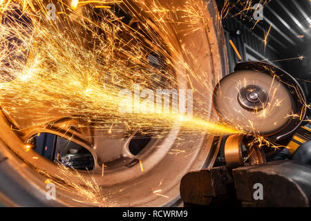 Eine Nahaufnahme von einem Automechaniker mit einem Metall Grinder Lager in einer Werkstatt zu schneiden, helle Blitze fliegen in verschiedene Richtungen. Die Arbeit der Aut. Stockfoto