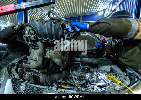 Nahaufnahme der Einbau des Motors in ein altes Auto mit einem pneumatischen manuelle Kran in der Werkstatt. Die Arbeit von Automechaniker bis t entfernen Stockfoto