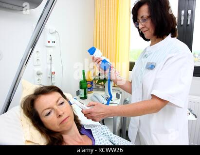 Krankenschwester mit einem digitalen Thermometer, um die Körpertemperatur eines Patienten in einem Krankenhausbett zu messen Stockfoto