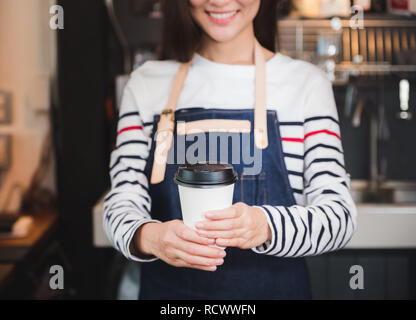 Asiatische Frau barista Schürze tragen Jean Holding heiße Tasse Kaffee serviert zu Kunden mit lächelnden Gesicht an der Theke, Cafe Restaurant Service Konzept. waitres Stockfoto