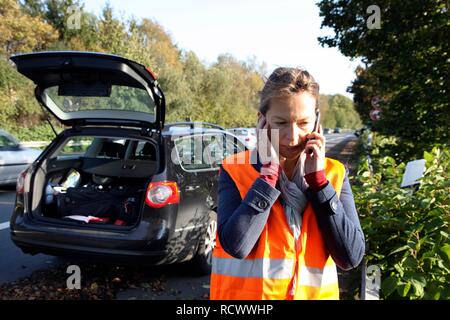 Autopanne, weibliche Fahrer hat auf der Standspur eines Landes Straße angehalten, das Tragen einer Warnweste, macht Hilfe rufen Stockfoto