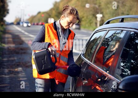 Autopanne, weibliche Fahrer hat auf der Standspur eines Landes Straße angehalten, das Tragen einer Warnweste, Nachfüllen von leeren Stockfoto