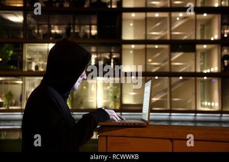 Hacker arbeitet an einem Laptop Computer vor einer kommerziellen Gebäude, dass Hacker in das Netzwerk des Unternehmens, symbolische Bild für Stockfoto