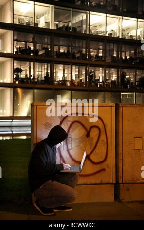 Hacker arbeitet an einem Laptop Computer vor einer kommerziellen Gebäude, dass Hacker in das Netzwerk des Unternehmens, symbolische Bild für Stockfoto