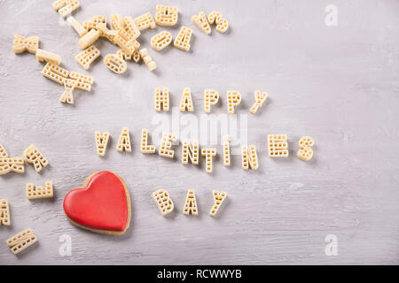 Text Valentines Tag mit Makkaroni in Form von Briefen und einem roten Herzen auf grau Holztisch geschrieben Stockfoto