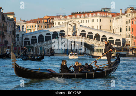 Venedig, Italien, 20. März 2018: Venezianische Gondoliere, Touristen auf der Gondel am Grand Canal und die Rialto Brücke im Hintergrund Stockfoto