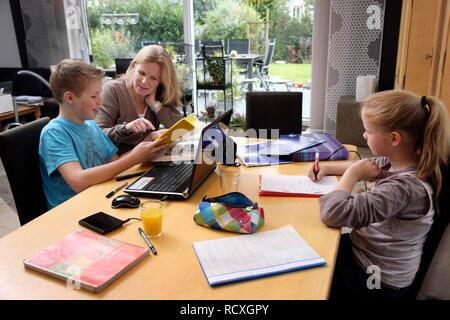 Geschwister ihre Hausaufgaben im Wohnzimmer, ihre Mutter ist Ihnen zu helfen Stockfoto