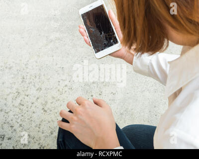 Frau Kommissionierung gebrochen Smart Phone aus dem Boden Stockfoto
