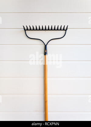 Minimalistisches Bild der neuen Rechen hängen an sauberen weißen Holz- Struktur Wand, Vertikal Stockfoto