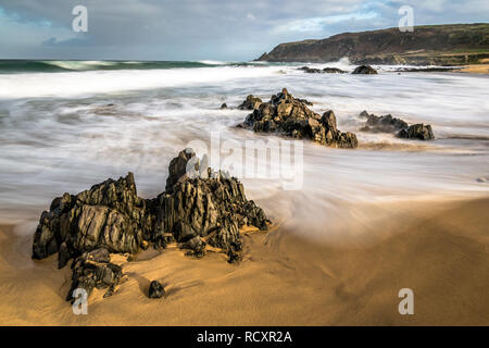 Verschwommenes Wellen zusammenhaengen Felsen an einem Sandstrand in Irland. Stockfoto