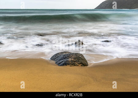 Einen Felsen auf einem sandigen Strand mit watter Schäumen und Wellen in der vom Meer kommenden Stockfoto