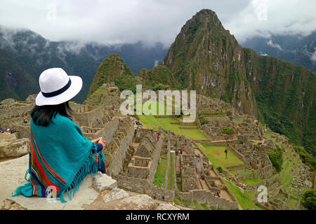 Weibliche Reisende Sitzen auf der Klippe an der Inka Ruinen von Machu Picchu, UNESCO Weltkulturerbe in der Provinz Cusco Region, Urubamba, Peru Suchen Stockfoto
