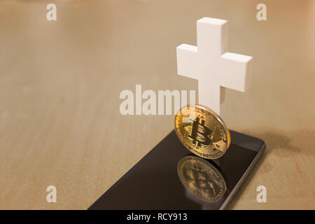 Tot Bitcoin Konzept mit einem weißen Kreuz und Smartphone als Grab Stockfoto