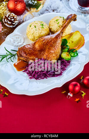 Festliche gebratene Gans drumstick zu feiern Weihnachten hohen Winkel auf Rot mit decortions mit Rosenkohl, Rotkohl und Knödel serviert gesehen Stockfoto