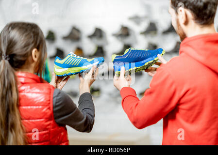 Der Mann und die Frau der Wahl Schuhe für Wandern, stehen im modernen Sport Shop mit schönen Schaukasten auf dem Hintergrund Stockfoto