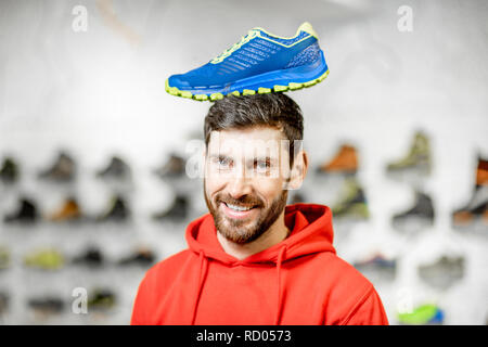 Lustige Porträt eines Mannes mit Sport Schuh auf dem Kopf stehend im Sport Shop Stockfoto