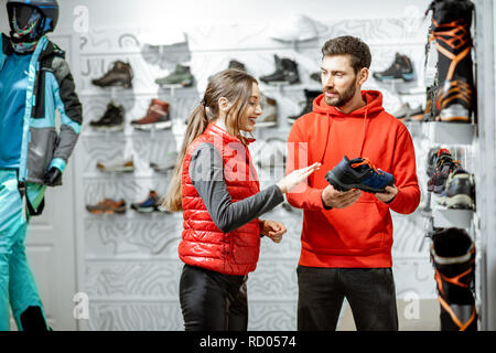 Mam und Frau in Rot Sport Kleidung wählen trail Schuhe für Wanderungen stehen in der Nähe des showacase des modernen Sports Shop Stockfoto