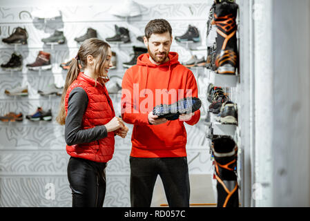 Mam und Frau in Rot Sport Kleidung wählen trail Schuhe für Wanderungen stehen in der Nähe des showacase des modernen Sports Shop Stockfoto